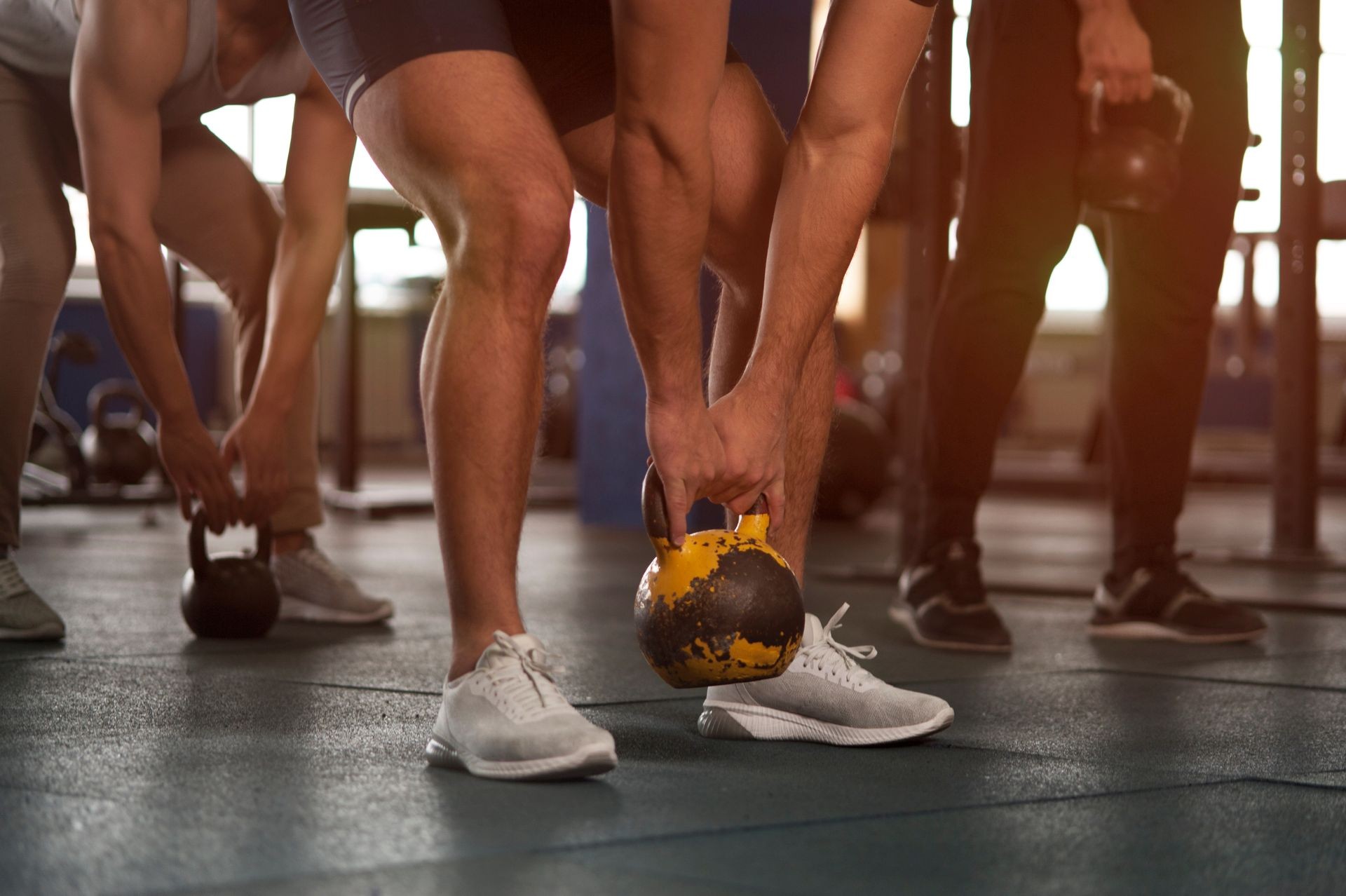 Young People in Gym Training With Kettlebells. Side View - Small Group of Male Athletes During Workout. Sports, Fitness, Healthy Lifestyle and Teamwork